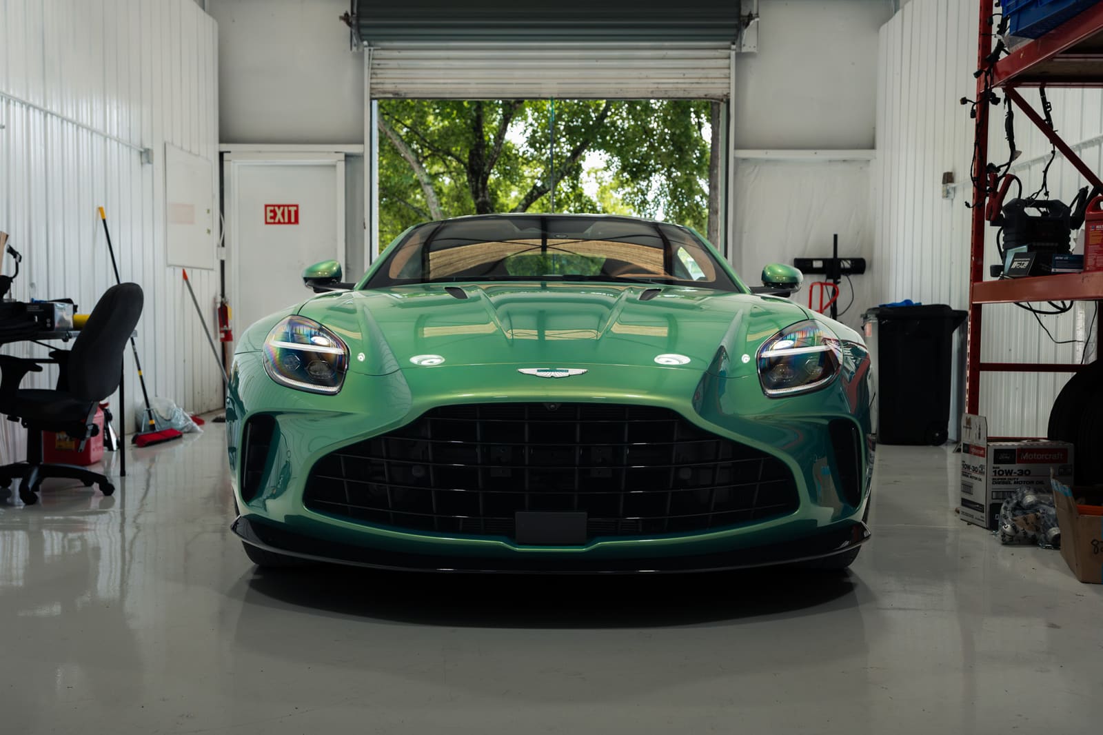 Green Aston Martin Vantage parked nose out in a bay at the Eurocharged Atlanta shop, the roll-up door open behind it