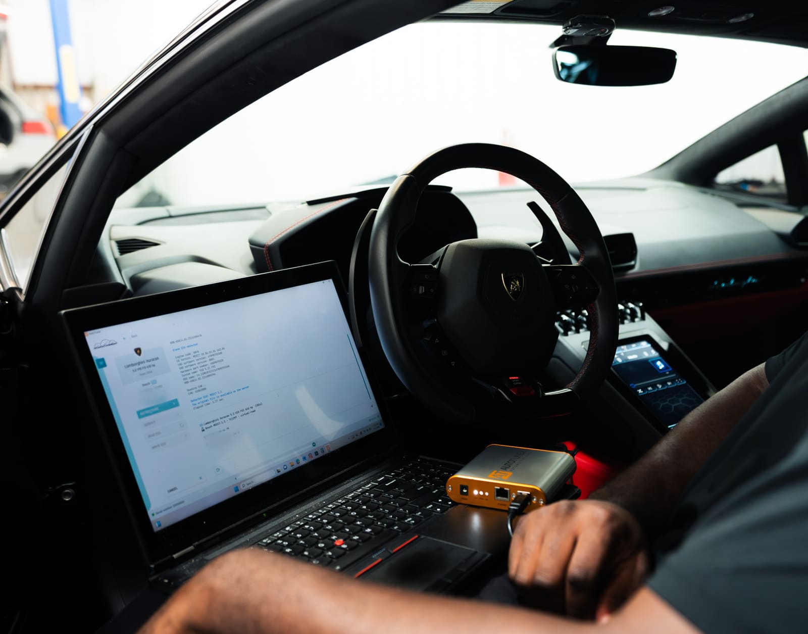 A technician’s hands at a laptop and an AutoTuner interface inside a Lamborghini Huracán