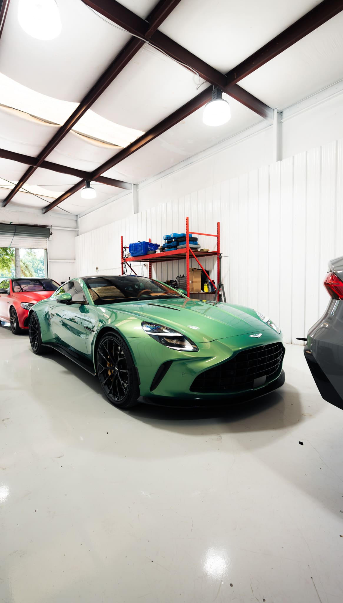 Green Aston Martin Vantage on the shop floor at Eurocharged Atlanta, with a red sedan parked behind it